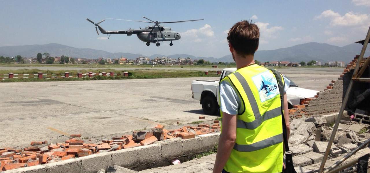 A man wearing an ACS vest looks on as a helicopter leaves an airfield with humanitarian aid for victims of the Nepalese earthquake in 2015